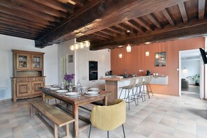 A dining area with a wooden table, benches, and chairs, a kitchen with modern appliances, and a wooden ceiling. - L'Etang Guillaume - Avec Jacuzzi, jardin de 5000m2 (Poilley)