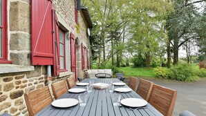 Ein Essbereich im Freien mit einem Steinhaus, roten Fensterläden und einem Tisch für sechs Personen.