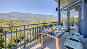 A balcony with a table set for dining, a view of a mountainous landscape, and a glass door leading to an outdoor area.