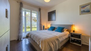 A bedroom with a bed, bedside tables, a nightstand, a window with curtains, and a painting on the wall.