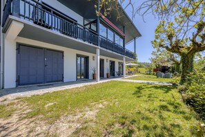 A modern two-story house with a balcony, garage doors, and a well-maintained lawn.