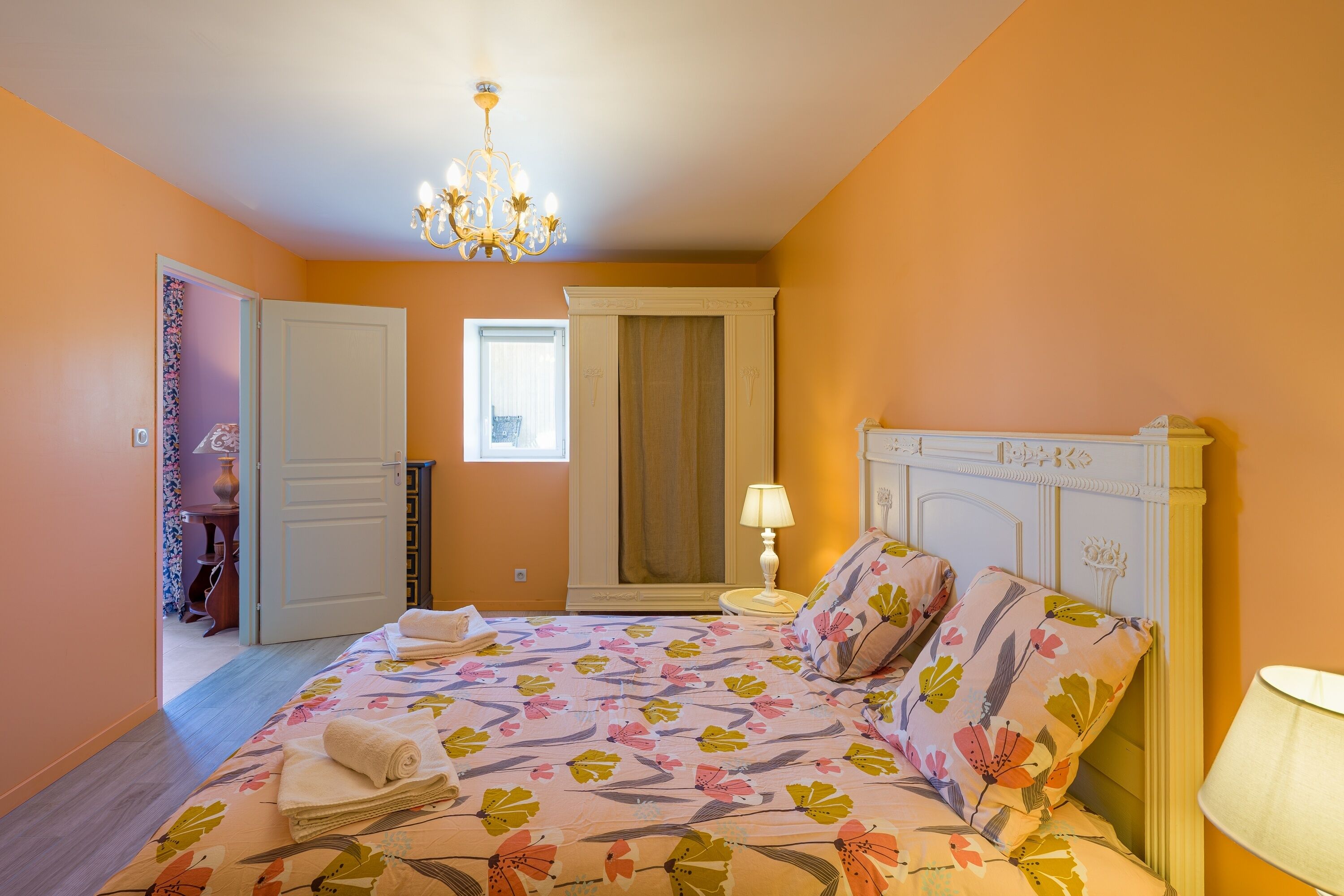 Ein Schlafzimmer mit Bett, einer Deckenleuchte, einem Nachttisch und einer Tür zu einem anderen Raum.