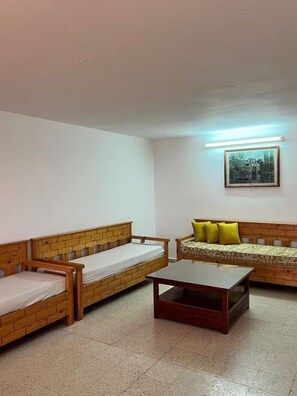 Une pièce avec deux lits en bois, un canapé avec des coussins jaunes, une table et un tableau encadré au mur.