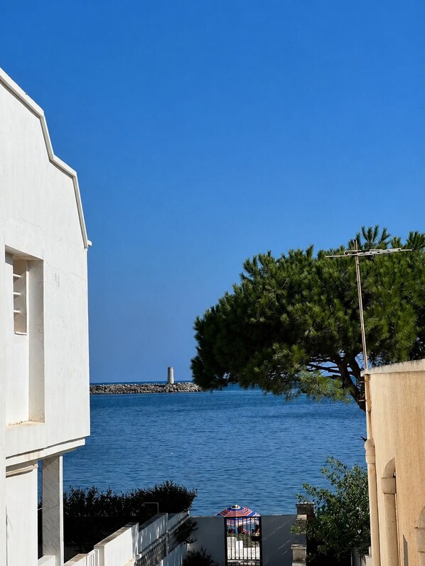 A coastal view with a white building, a tree, and a distant lighthouse.