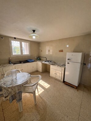A kitchen with a dining table, chairs, a refrigerator, a stove, and a window with bars.