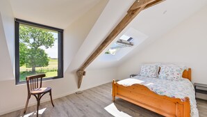 Una camera da letto con soffitto spiovente, un letto di legno, una sedia e una finestra con vista su un albero.