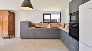 Una cucina moderna con mobili grigi, un piano di lavoro in legno, un lavello, un forno Bosch e una finestra con vista su un edificio.