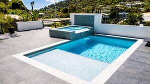 Une piscine rectangulaire dont le bord est recouvert de carrelage, entourée d’une terrasse également carrelée, de couleur grise.