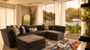 Una sala moderna con un sofá seccional, un ventanal con vistas a una colina y una planta decorativa.