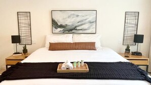 Ein Hotelzimmer mit einem Bett, zwei Nachttischen, einem Tablett mit Pflegeprodukten und abstrakter Wandkunst.