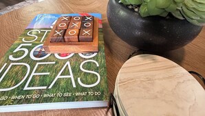 Taula amb un llibre anomenat 'ST 500 IDEAS', un trencaclosques de fusta i una planta en test.