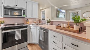 A modern kitchen with white cabinetry, a built-in microwave, a stove, and a sink. - Charming CDA Cottage · Walk to Downtown & the Lake (Coeur d'Alene)