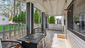 A covered porch with a table and chairs, a view of the backyard, and a house in the background. - Charming CDA Cottage · Walk to Downtown & the Lake (Coeur d'Alene)