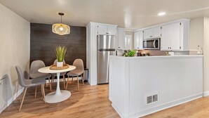 A modern kitchen with white cabinetry, a stainless steel refrigerator, a microwave, and a dining area with a round table and chairs. - Charming CDA Cottage · Walk to Downtown & the Lake (Coeur d'Alene)