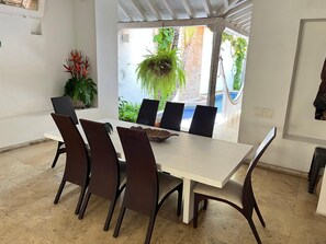 A meeting room with a white table, dark chairs, a small plant, and a view of a pool and greenery outside. - CASA MARIA CARTAGENA (Cartagena)
