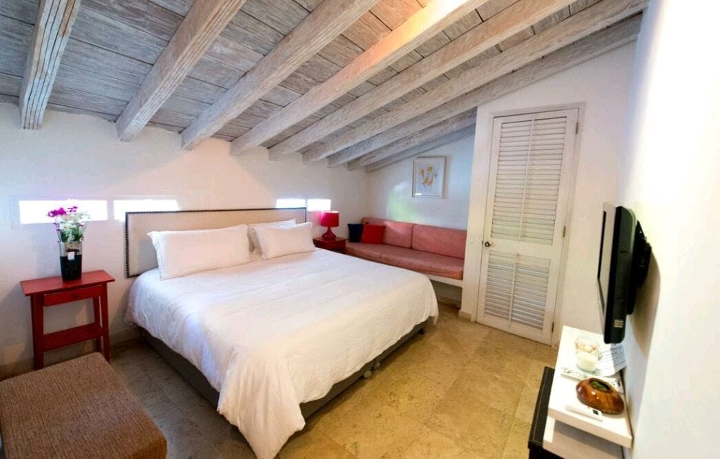 Un dormitorio con una cama grande, una mesita de noche roja, un sofá rojo, una puerta blanca y un techo de madera.