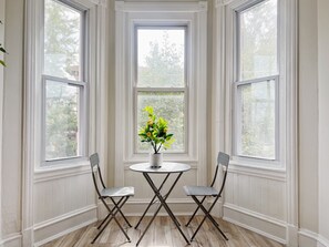 Ein Zimmer mit drei großen Fenstern, einem runden Tisch mit zwei Stühlen und einem Blumentopf.