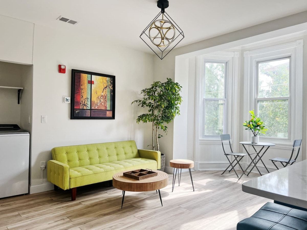 A modern living room with a green sofa, a round wooden coffee table, and a dining area with a table and chairs.