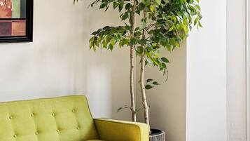 A room with a green sofa, a wooden coffee table, a potted plant, and a painting on the wall.