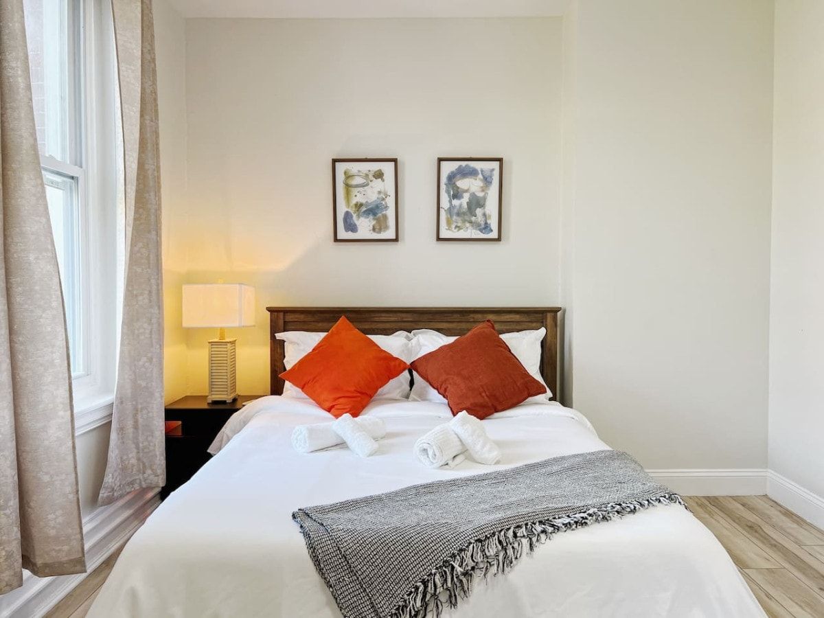Ett hotellrum med en säng, kuddar, en lampa och två inramade tavlor på väggen.