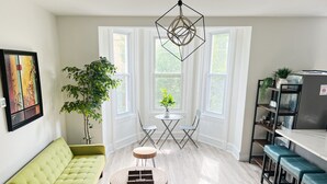 A bright, modern kitchen with a dining area, a green sofa, and a large window providing natural light. - Ramblei near Drexel Park: 6-Bedroom Unit B (Philadelphia)