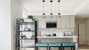 A modern kitchen with white cabinets, a black microwave, and a central island with bar stools. - Ramblei near Drexel Park: 6-Bedroom Unit B (Philadelphia)