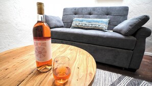 Eine Flasche Arizona Rose Wein und ein Glas auf einem Holztisch in einem Wohnzimmer mit grauem Sofa und gemusterten Kissen.