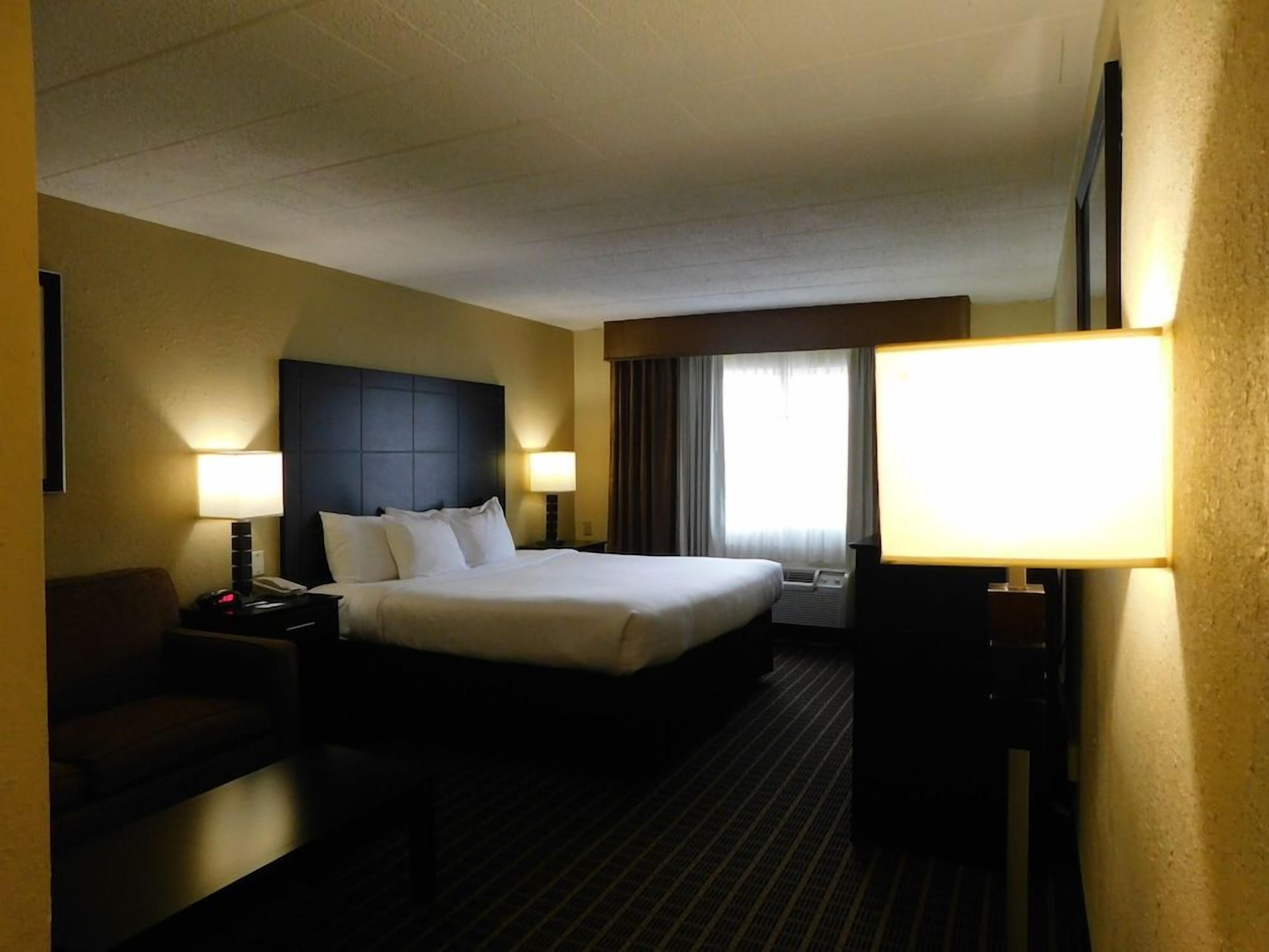 A hotel room with a large bed, two bedside tables with lamps, a flat-screen TV, and a window with curtains.