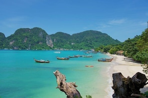 A beach with boats, clear turquoise water, and lush green mountains in the background. - Bay View Resort Koh Phi Phi (Ko Phi Phi)