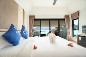 Hotelkamer met een groot bed, twee blauwe kussens, een witte spreidek, een rode bloem, een wit pluche dier, een televisie en uitzicht op het landschap door grote ramen.