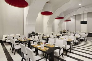 A dining area with white chairs, black tables, and red accents on the ceiling. - Saura Hotel Agra A Club Mahindra (Agra)