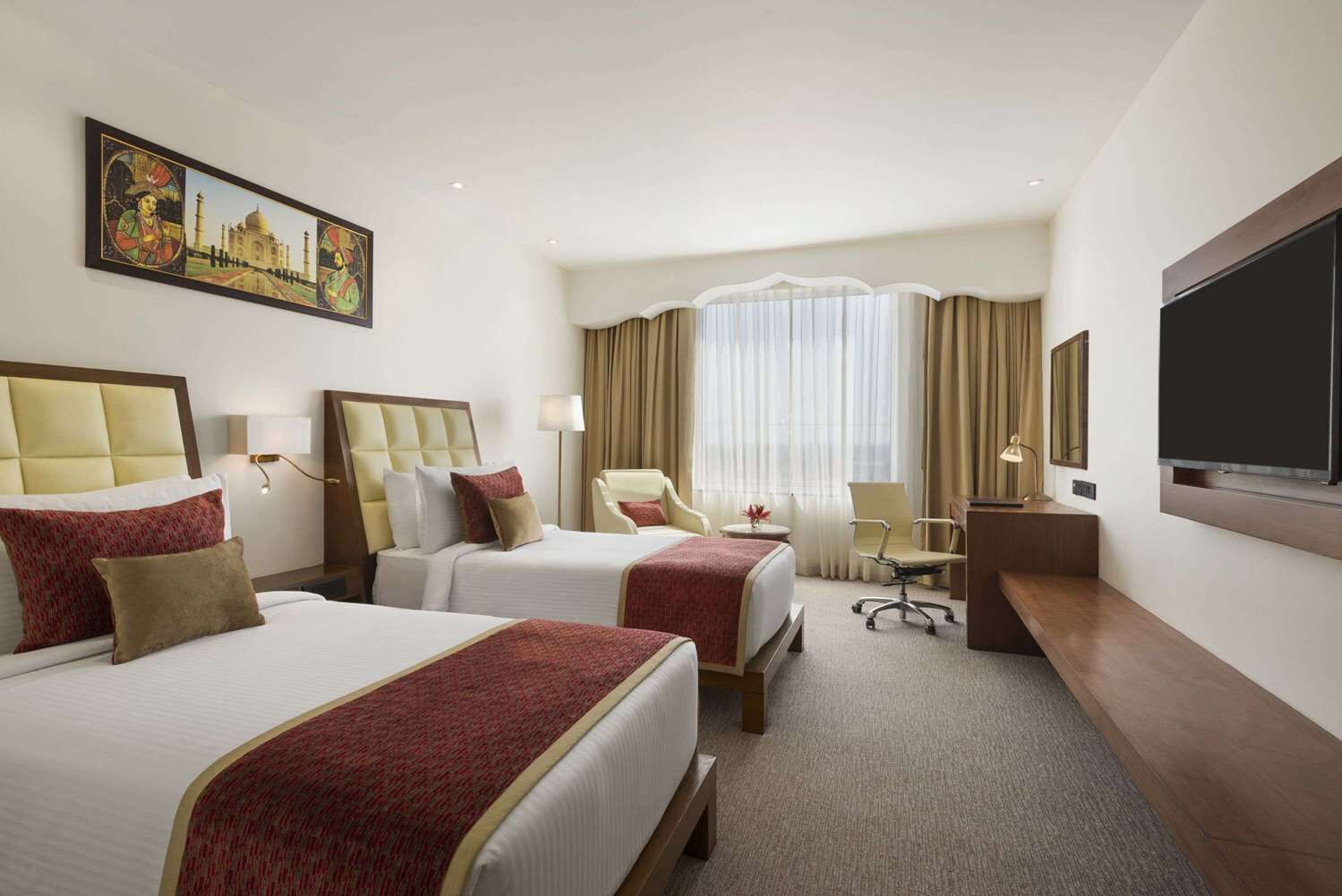 A hotel room with two beds, a desk, a chair, a television, and a large window with curtains.