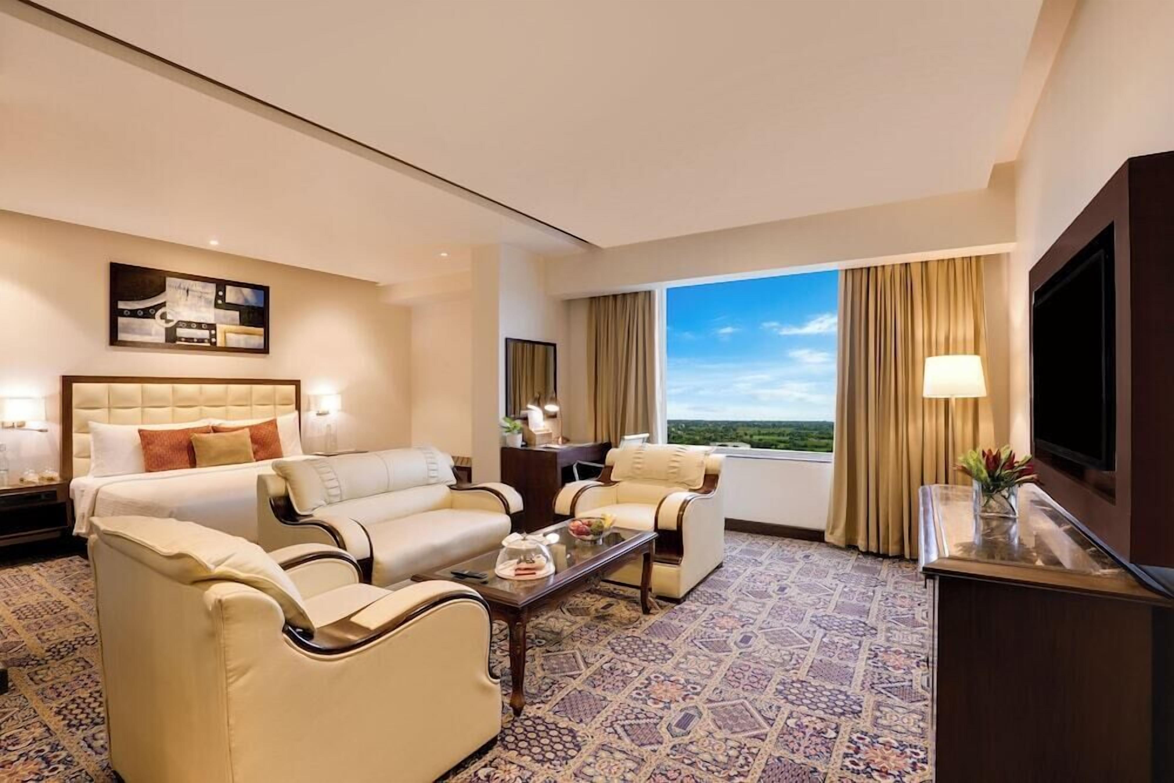 A hotel room with a large bed, two sofas, a coffee table, and a TV.