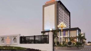 A modern hotel with a prominent entrance, a decorative light fixture, and a sign indicating it is a Ramada Plaza. - Saura Hotel Agra A Club Mahindra (Agra)