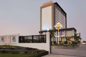 A modern hotel with a prominent entrance, a decorative light fixture, and a sign indicating it is a Ramada Plaza. - Saura Hotel Agra A Club Mahindra (Agra)