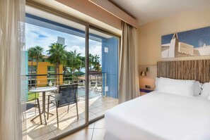 Ein Hotelzimmer mit Bett, einem Balkon mit Tisch und Stühlen und Blick auf Gebäude und Palmen.