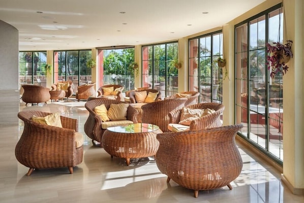 A spacious indoor area with wicker furniture and large windows. - Occidental Menorca (Sant Lluis)
