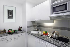 A modern kitchen with white cabinets, a granite countertop, a built-in microwave, and a kettle. - Citadines City Centre Lille (Lille)