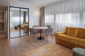 A modern living room with a round table, four chairs, a sofa, and a large window with curtains. - Residence Inn by Marriott Lille (Lille)