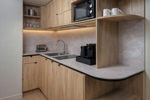 A modern kitchen with wooden cabinets, a microwave, a coffee maker, and a sink. - Citadines City Centre Lille (Lille)
