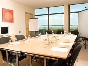 Ein Konferenzraum mit langem Tisch, Stühlen, einer Whiteboard, einer Projektionsleinwand und einem Fenster mit Blick.
