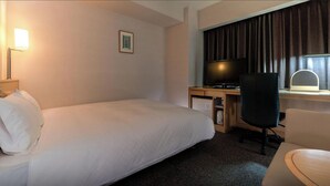 Habitación de hotel con una cama individual, un escritorio con silla, televisión y un refrigerador pequeño.