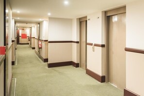 Ein Hotelgang mit Teppichböden, Türen und einem Feuerlöscher.