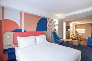 Et moderne hotelværelse med en stor seng, et skrivebord, en stol og et lille tekøkken.