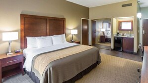 A hotel room with a large bed, bedside tables, a desk, a mirror, and a bathroom visible through an open door.