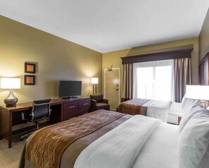 Habitación de hotel con dos camas, un escritorio con silla, un televisor y una ventana con cortinas.