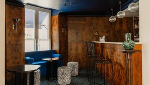 Un área de bar acogedora con un sofá azul, otomanas a rayas de cebra y un jarrón verde sobre un pedestal.