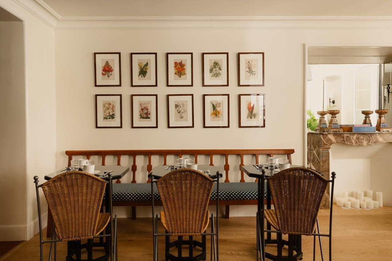 A dining area with a bench and chairs, framed botanical prints on the wall, and a fireplace with candles.