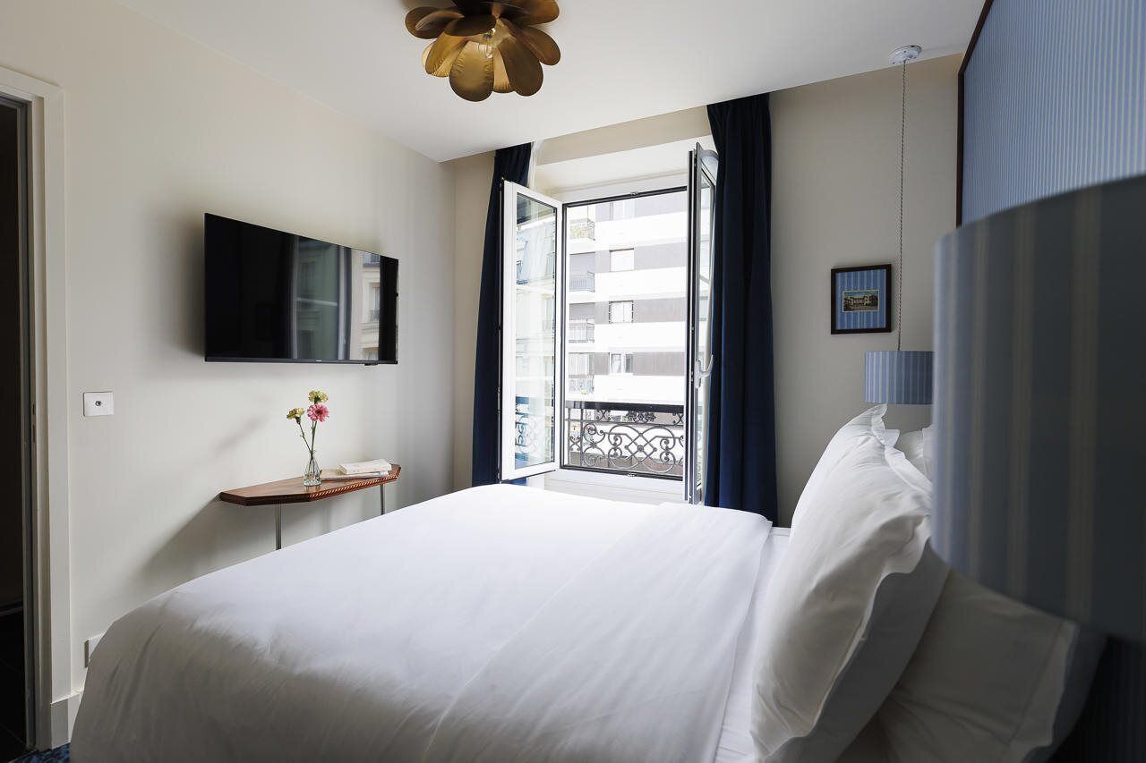 Ein Hotelzimmer mit Bett, Wand-Fernseher, Nachttisch mit Blumenvase und Blick auf den Balkon.