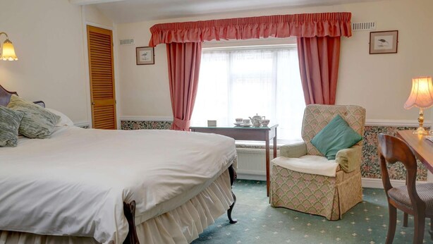 A hotel room with a large bed, a chair, a small table with a lamp, and a window with curtains. - The Bell In Driffield (Driffield)